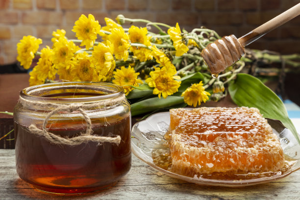 蜂房里放着蜂蜜，一个木勺，一罐蜂蜜，一朵黄色的非洲菊花。图片下载