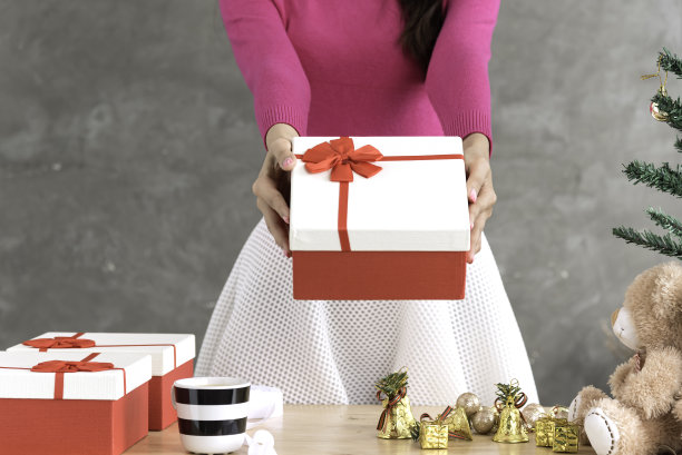 亚洲妇女在家里装饰圣诞树。挂金戒指，手捧礼盒。图片下载