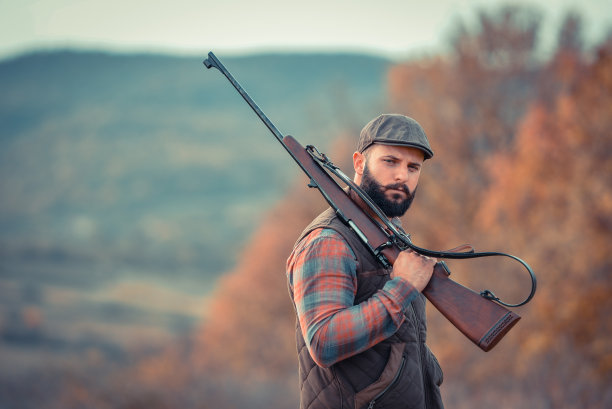 年轻强壮的黑胡子猎人，手里拿着枪，沿着土路走着图片下载