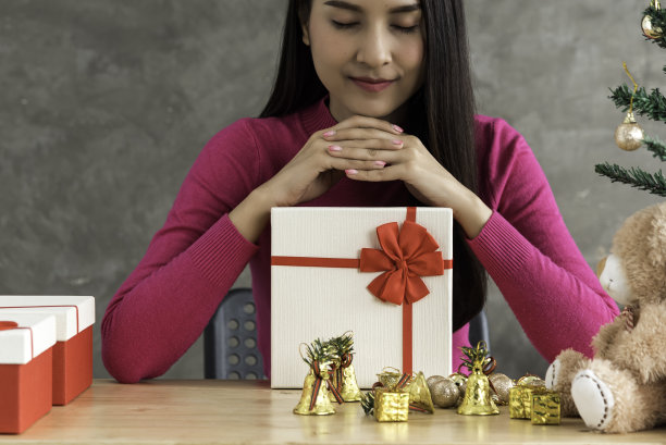 亚洲妇女在家里装饰圣诞树。挂着金戒指，希望和祈祷。图片下载