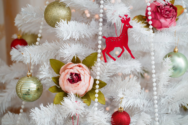 美丽的装饰品挂在一棵白色的人造圣诞树上。绿色的球，花，珠子，木鹿。节日的库存图片图片下载