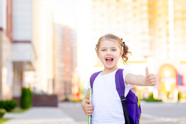 回到学校，一年级的女生背着书包，手里拿着一本书，高高兴兴地为全班同学竖起了大拇指图片下载