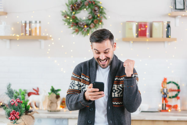 年轻的男性自由职业者商人庆祝胜利快乐的胜利读伟大的消息在家里的手机在新年和圣诞节假期图片下载