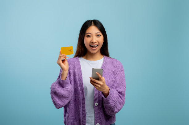 网上购物的概念。兴奋的亚洲女士与手机和信用卡在网上购买蓝色背景图片下载