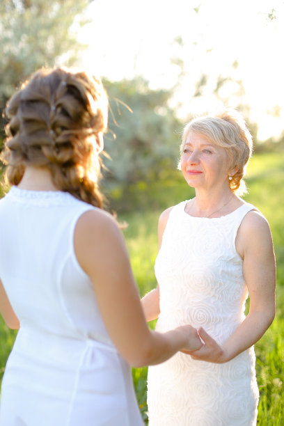 金发妈妈牵着女儿的手，穿着白色的裙子图片下载