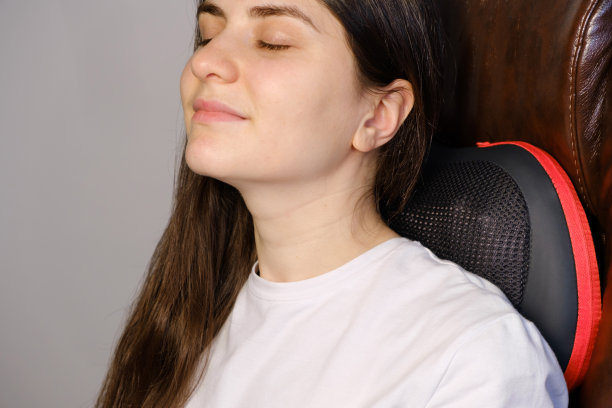 一个女人坐在带着按摩枕头的椅子上做颈部按摩。图片下载