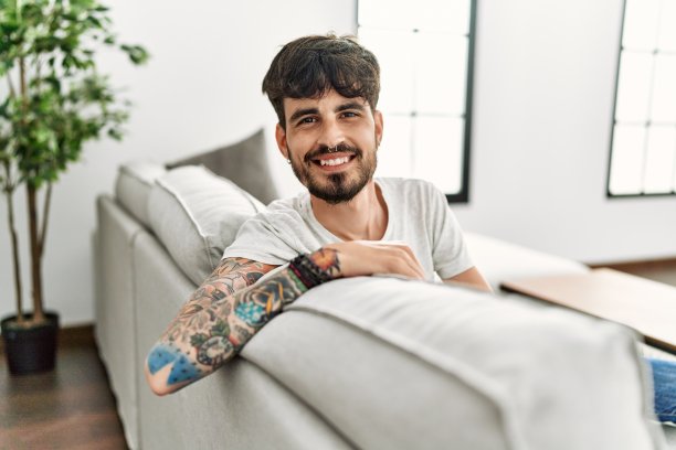 年轻的西班牙裔男子自信地微笑着坐在家里的沙发上图片下载