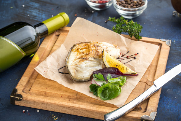 烤白鱼片放在木板上，蓝色背景上放一瓶葡萄酒图片下载