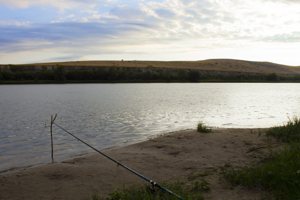晚上在河边钓鱼。一个安静而荒凉的钓鱼的地方。河上日落，黄昏。傍晚的风景，一条河和一根鱼竿。图片下载