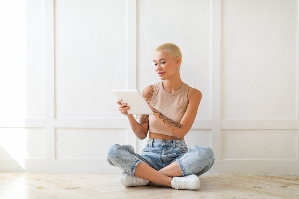 兴奋的年轻女士用平板电脑浏览互联网，坐在白墙上的地板上，自由空间图片下载