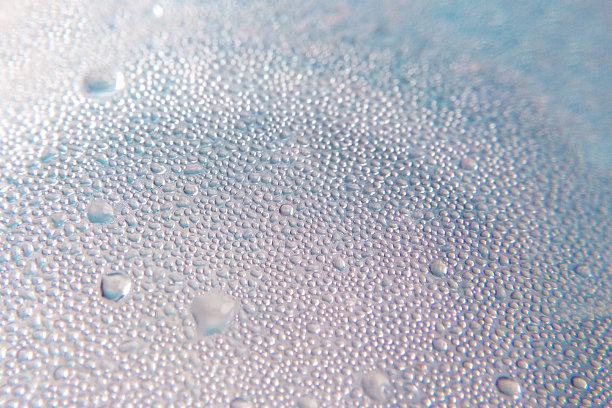 一滴水珠滴在玻璃表面，蓝色色调的特写模糊了背景图片下载