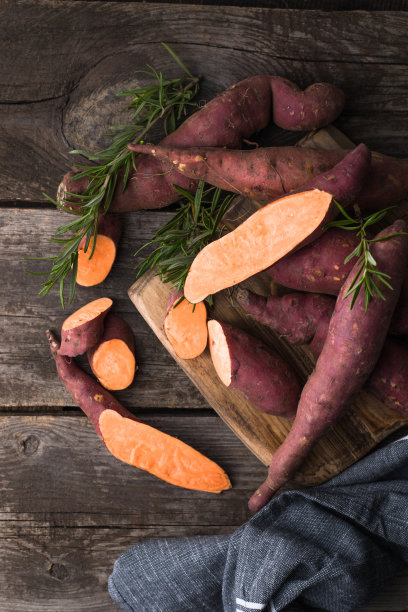 红薯在木板背景上，特写。生红薯或加香草的薯片图片下载