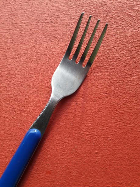 红色背景上蓝色手柄的不锈钢叉子图片下载