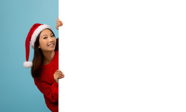 圣诞节的报价。兴奋的亚洲女士在圣诞老人的帽子持有白色空广告板在蓝色的工作室背景图片下载
