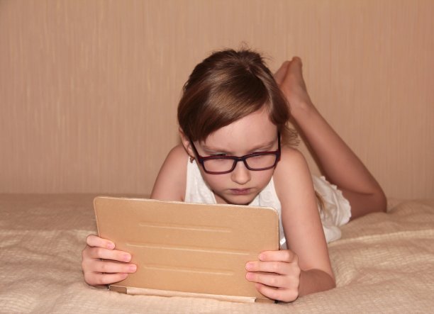 孩子躺在床上玩平板电脑。图片下载