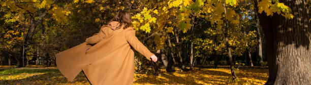 一个穿着大衣的女人正打着旗子奔跑，双臂伸在秋日阳光明媚的森林里。本空间图片下载