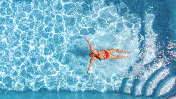 活跃的年轻女孩在游泳池空中无人机从上面的观点，年轻的女人游泳在蓝色的水游泳池，热带度假胜地图片下载