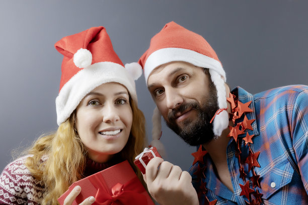 一男一女戴着圣诞帽，手里拿着红色的礼品盒。节日的海报素材图片