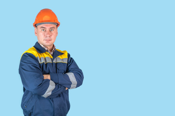 一名戴着橙色头盔的工人双手交叉站在蓝色背景上，copyspace图片下载