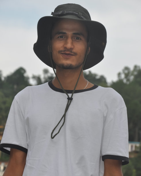 一个印度年轻人站在户外，头戴乡村帽，身穿白色t恤，看着镜头图片下载