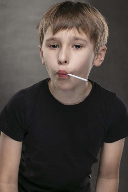 拿着棒棒糖的滑稽男孩。时尚的孩子在灰色的背景。一个穿着黑色t恤的十岁小孩。图片下载