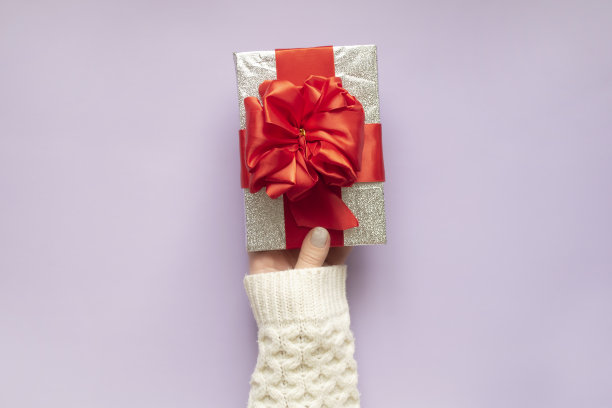穿着白色毛衣的女人拿着一个有红丝带的礼品盒。模板,布局。图片下载