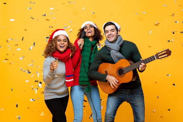 一组快乐的不同的亲密朋友有派对唱歌和庆祝圣诞节在黄色工作室背景与五彩纸屑图片下载