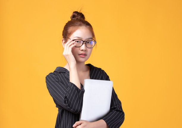 快乐随意的亚洲女孩的肖像与笔记本电脑孤立在黄色背景。回到学校，学习观念。图片下载