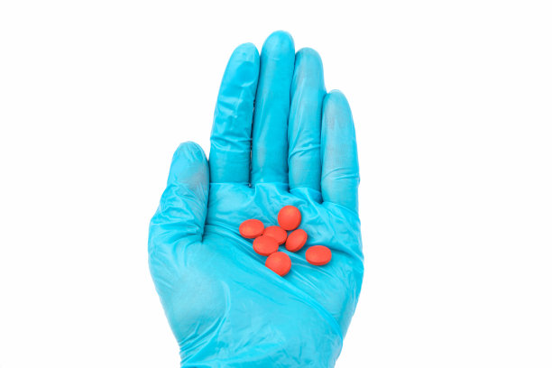 手医生戴着医用蓝手套拿着红色药丸。药物研究的概念。图片下载