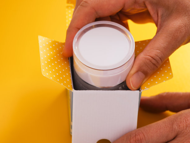 一位妇女从一个黄色背景的盒子里拿出面霜。图片下载