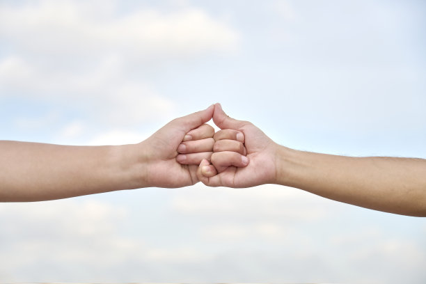 两个男人的手指勾在一起，前面是模糊的天空背景图片下载