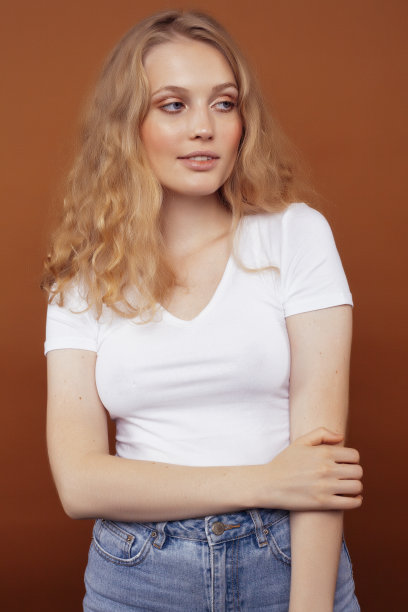 年轻漂亮的金发卷发女孩在棕色背景下摆出欢快的姿势，生活方式让人产生了观念图片下载