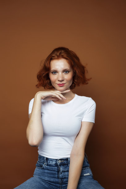 年轻漂亮的红发女孩在温暖的棕色背景下摆着欢快的姿势，生活方式让人眼前一亮图片下载