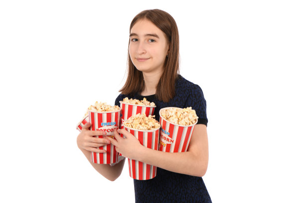 一个美丽的女孩的肖像拿着一桶爆米花站在白色。图片下载