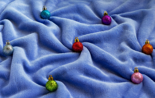 在蓝色皱巴巴的毛皮织物上，有闪亮明亮的圣诞树装饰小玩意的静物构图。图片下载
