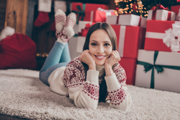 甜蜜年轻女士的全身照片躺在地毯附近的礼物树穿毛衣牛仔裤袜子在家里过圣诞节图片下载