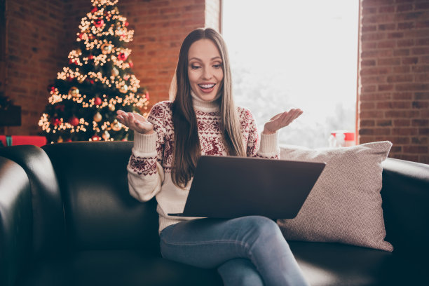 照片:时髦的成熟女士坐着谈笔记本电脑，穿着针织衫，牛仔裤在家里过新年图片下载
