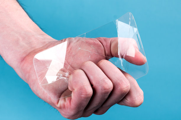 蓝色背景下，一名男子手持破碎的智能手机安全玻璃。易碎设备概念图片下载