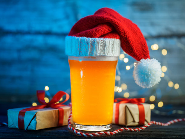 戴着圣诞老人帽子的啤酒。圣诞礼品盒，蓝色背景图片下载