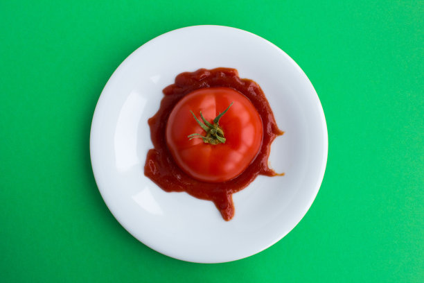 在绿色背景的白色盘子上，放入番茄酱的番茄切片。前视图。特写镜头。图片下载