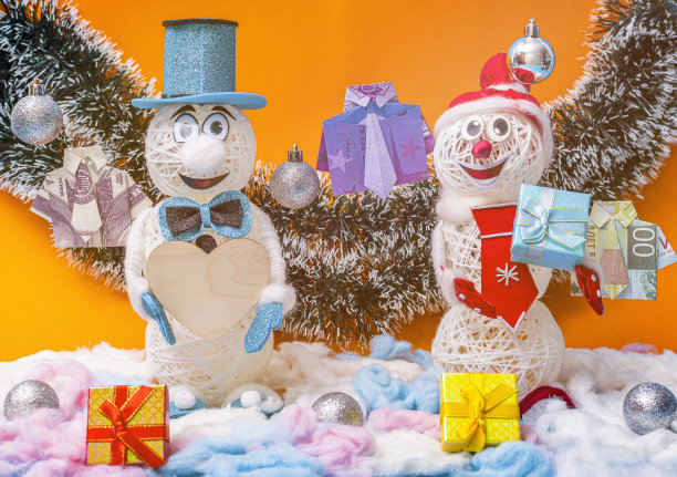 两个顽皮有趣的圣诞雪人拿着木心和礼品盒。站在橙色的背景上。图片下载