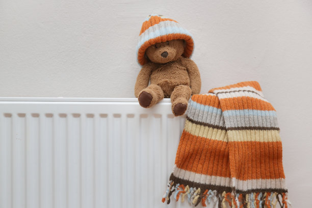 泰迪熊和小孩的羊毛帽子和围巾在暖气片上晾干的照片。冬季的概念。图片下载