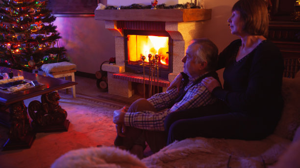 一对年老的夫妇坐在黑暗的房间的壁炉前图片下载