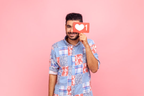 穿着蓝色休闲衬衫的微笑男人躲在红色点赞计数器后面，对着镜头露出微笑，社交网络中的SMM管理图片下载