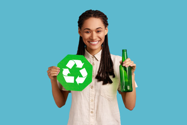 一个留着长发绺的女人拿着回收标志和玻璃瓶，面带微笑地看着镜头。图片下载