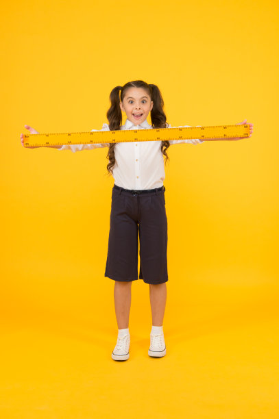 好长的尺子啊。惊讶的小学生拿着硬木尺在黄色的背景上。小孩用公制尺测量。我的尺子有一米长图片下载
