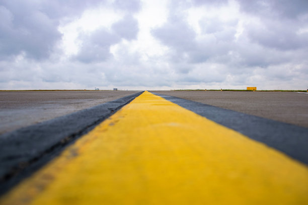 特写黄黑相间的跑道标志在机场的混凝土上延伸到引人注目的蓝天(选择性聚焦)图片下载