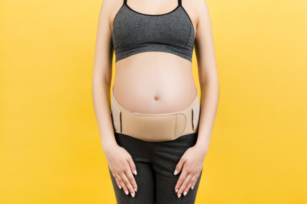 裁剪图像的怀孕带穿在怀孕妇女减少疼痛在黄色背景与复制空间的背部。骨科腹部支持带的概念图片下载