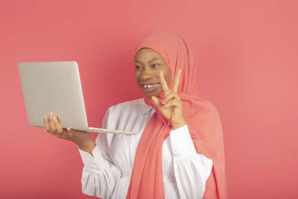 非裔美国妇女在笔记本电脑屏幕上挥舞着粉色围巾，在粉红色背景上进行视频通话图片下载