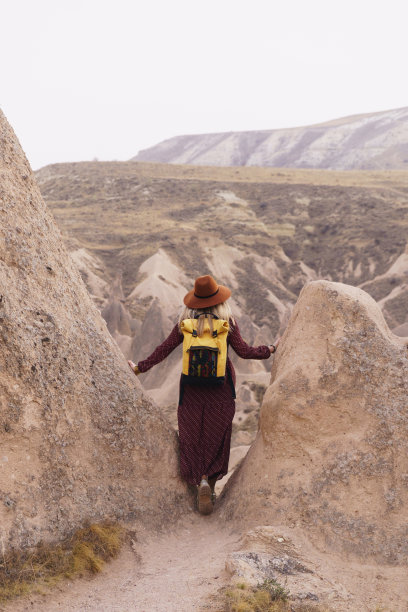 戴着棕色帽子，穿着长裙的旅行妇女在沙漠山谷和岩石中行走。旅游和漫游的概念。卡帕多西亚,土耳其。图片下载